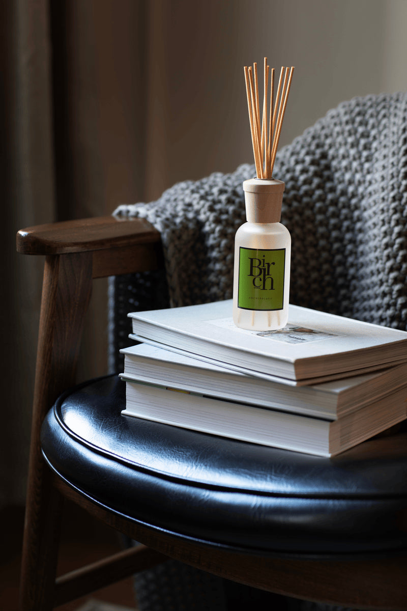 Diffuser bottle with reeds on a stack of books on a chair - image 2