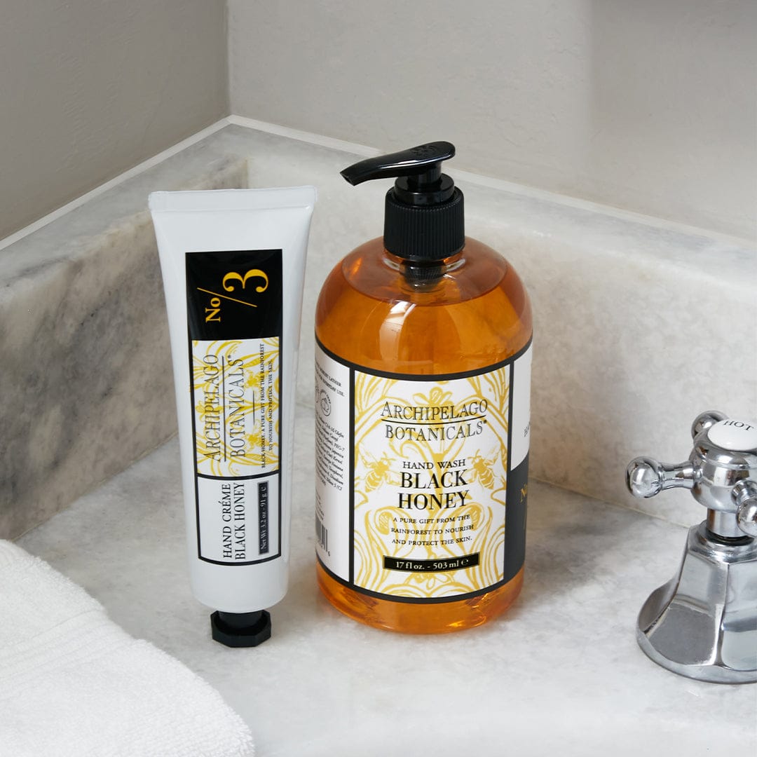 A tube of Black Honey Hand Creme sits on a marble bathroom countertop beside a chrome faucet and a neatly folded white towel, creating an inviting setting for luxurious hand moisturizer application and expert cuticle care. - image 2