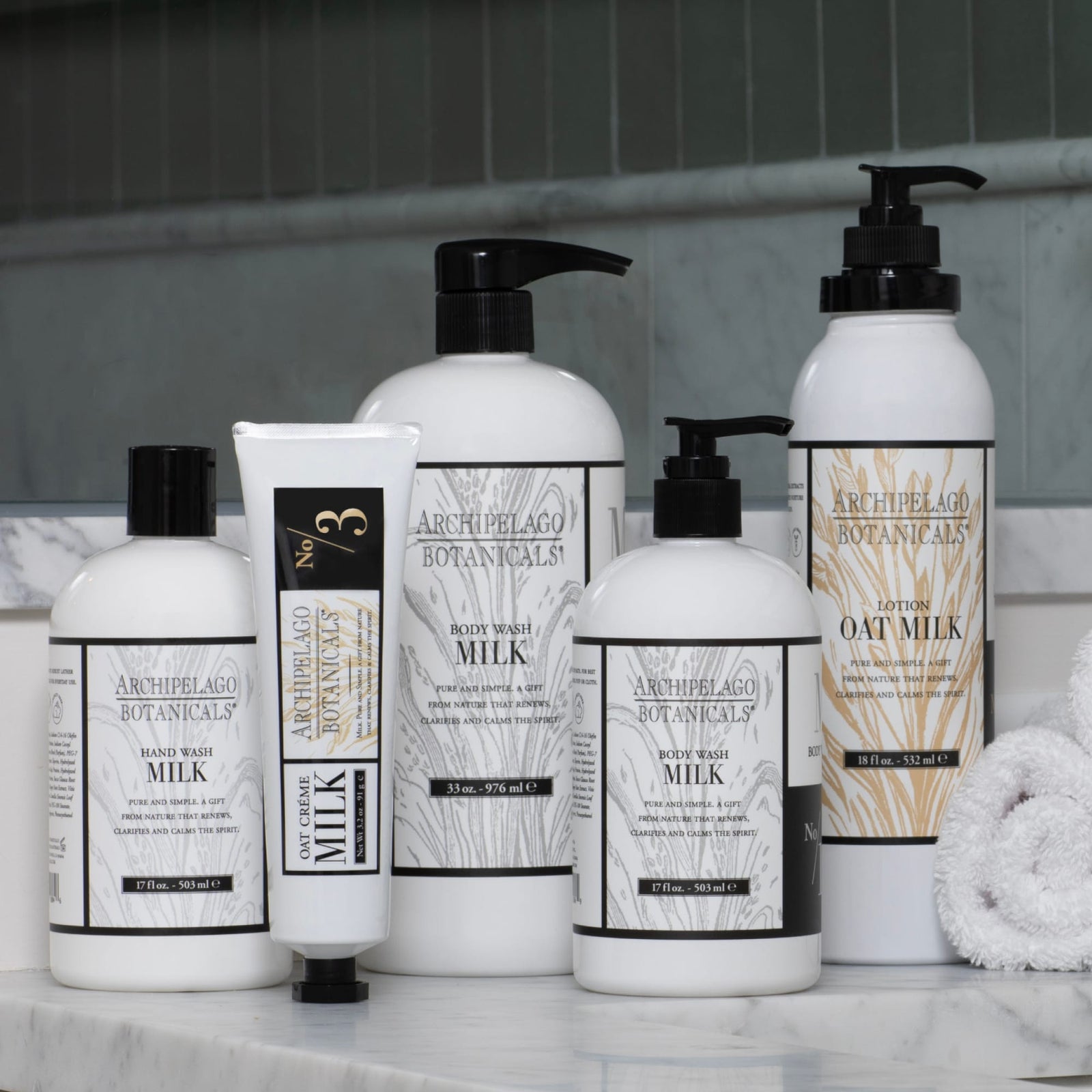 Sure! Here’s the rewritten sentence using the data you provided: The Oat Milk Body Lotion—enriched with hydrating jojoba esters—is arranged on a marble countertop next to two rolled white towels, with a tiled wall in the background. - image 7