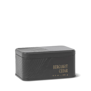 A rectangular black metal travel tin candle with an embossed texture and gold lettering displaying “BERGAMOT CEDAR 6.5 oz – 184 g” on the side. The closed lid keeps the fresh, herbaceous scent of the Bergamot Cedar Travel Tin Candle inside. - image 1