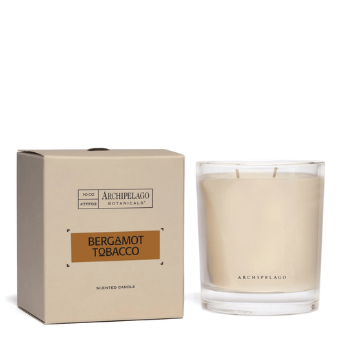 A beige box labeled "Bergamot Tobacco Credenza Candle" by Archipelago Botanicals sits beside a clear glass candle with white wax and two wicks, both promising an inviting bergamot aroma.
