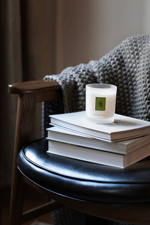 Candle on a stack of books with a textured chair and blanket in the background