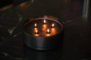A round, black Forest 5-Wick Candle with five lit wicks, sitting on a dark surface. - image 2