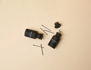 Two Black Forest Luxury Matches apothecary jars—one upright, one tipped over—sit on a beige background with premium matches scattered around. Each matte black jar has a label and a black lid, adding stylish décor to any space.3