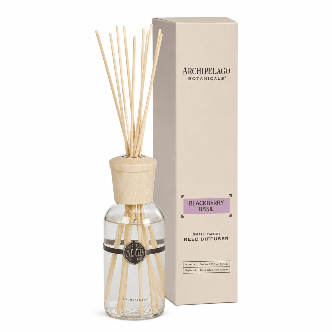 The Blackberry Basil Reed Diffuser with wooden sticks and cap stands next to its beige box, featuring a black logo on the glass bottle filled with a refreshing blackberry basil fragrance blend.1