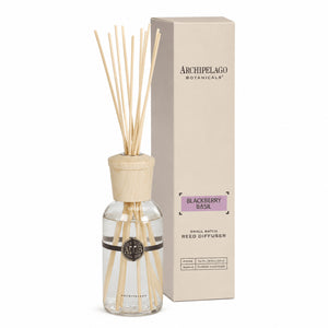 The Blackberry Basil Reed Diffuser with wooden sticks and cap stands next to its beige box, featuring a black logo on the glass bottle filled with a refreshing blackberry basil fragrance blend.1