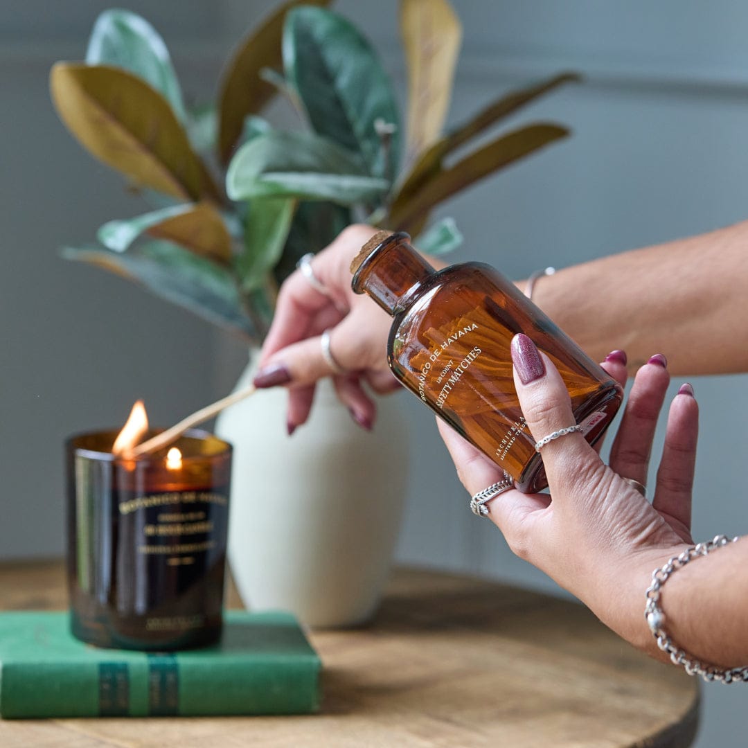 A bottle of Botanico de Havana matches being held in one hand with a candle being lit by the other hand.3