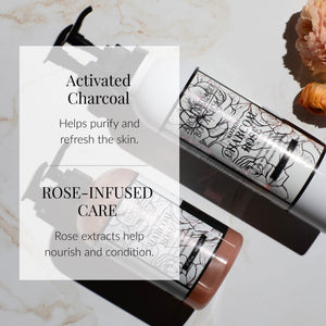 Two Charcoal Rose Body Lotion bottles rest on a marble surface—one standing upright, the other lying down—accompanied by delicate flowers. Text emphasizes Activated Charcoal for purification and rose extracts for nourishment. The lotion’s elegant, floral-themed packaging is showcased.6