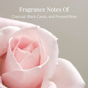 A close-up of a soft pink rose with text above it that reads, Fragrance Notes Of Charcoal, Black Cassis, and Pressed Rose. Inspired by the luxurious Charcoal Rose Body Lotion, this image captures the essence of a body lotion infused with Activated Charcoal for a deeply refreshing experience.4
