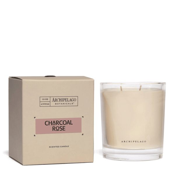 The Charcoal Rose Credenza Candle by Archipelago Botanicals, in a clear glass jar with minimalist black text, sits beside its matching box and fills the air with an elegant floral scent.