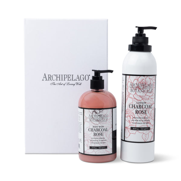 Two bottles from the Charcoal Rose Daily Ritual Gift Set, including lotion and bath & body wash with elegant floral labels, are displayed in front of a white Archipelago gift box.