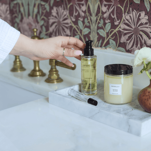 Hand reaching for body oil and scrub on bathroom counter 