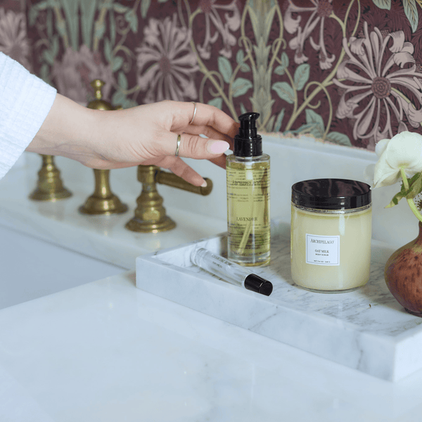Hand reaching for body oil and scrub on bathroom counter 