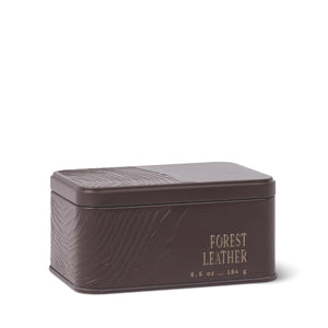 A rectangular brown metal tin labeled “Forest Leather Travel Tin Candle,” 6.5 oz (184 g), with a textured pattern on the lid and sides, features subtle sandalwood notes and is set against a white background. - image 1