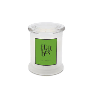 The Herbés Frosted Jar Candle is a white candle in a clear glass jar with a round lid. Its bright green “HERBES” label from ARCHIPELAGO hints at an herb garden scent, evoking the fresh aroma of Lemon Basil.1