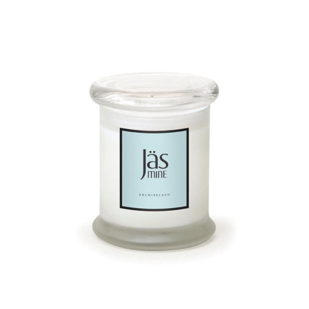 A Jasmine Frosted Jar Candle in a clear glass jar with a flat lid, lead-free cotton wick, and premium wax blend. The light blue label says “Jasmine” and “Archipelago.” Unused candle shown against a white backdrop.1