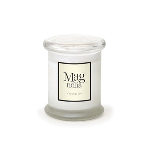 A white hand-poured Magnolia Frosted Jar Candle in a clear glass jar with a round lid. The cream label displays "Magnolia" and "Archipelago" in black, echoing classic apothecary candle style.1