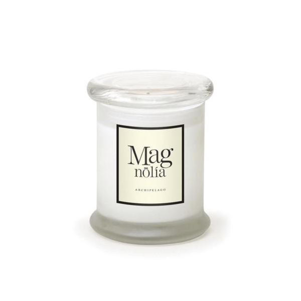 A white hand-poured Magnolia Frosted Jar Candle in a clear glass jar with a round lid. The cream label displays "Magnolia" and "Archipelago" in black, echoing classic apothecary candle style.