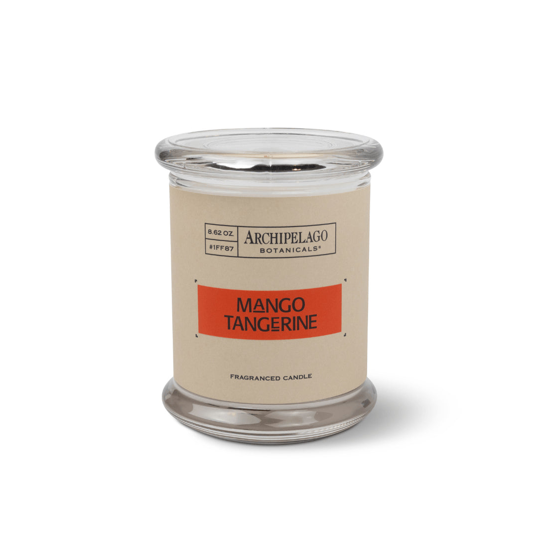 The Mango Tangerine Jar Candle, with a clear glass jar, tan label with orange stripe, and citrus-scented soy wax blend, is shown against a white background.1