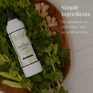 A bottle of Morning Mint Body Lotion sits on a wooden tray alongside fresh mint, cucumber, and ginger. Text reads: Simple Ingredients. Infused with essential oils for aromatherapy benefits. Free from parabens, phthalates, and artificial color.2