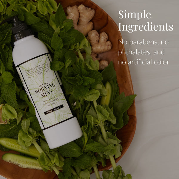 A bottle of Morning Mint Body Lotion sits on a wooden tray alongside fresh mint, cucumber, and ginger. Text reads: Simple Ingredients. Infused with essential oils for aromatherapy benefits. Free from parabens, phthalates, and artificial color.
