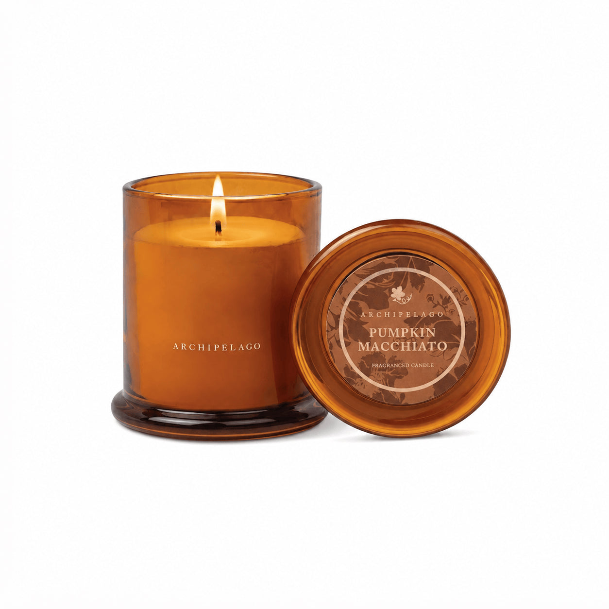 A lit amber glass hand-poured candle labeled Pumpkin Macchiato Jar Candle stands next to its lid, filling the air with a cozy autumn fragrance. - image 1