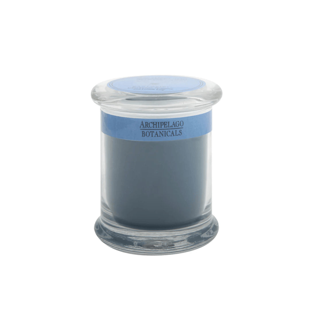 The Santorini Jar Candle features solid blue-gray wax infused with essential oils in a glass apothecary jar. It has a blue label reading Archipelago Botanicals and comes with a matching glass lid.1