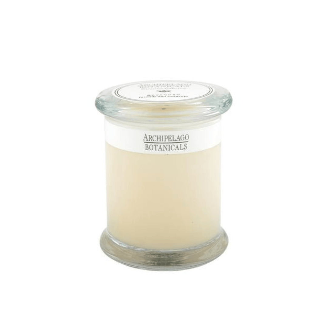 The Savannah Jar Candle is a clear glass apothecary-style candle with white wax and a glass lid. Its label reads Archipelago Botanicals, and it gently infuses the room with the fragrance of essential oils.1