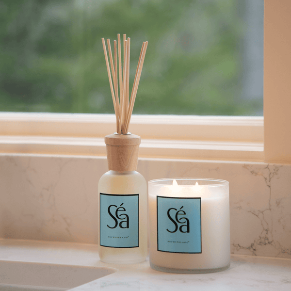 Séa diffuser and candle on a marble surface with a blurred greenery background