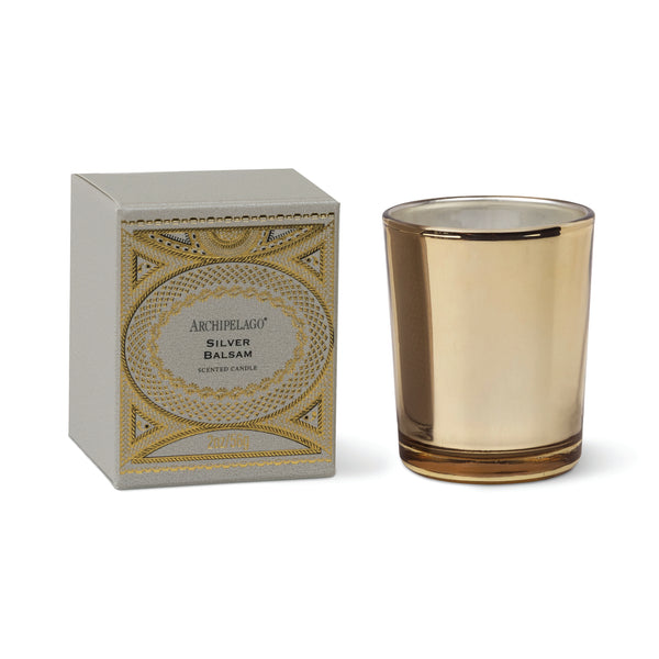 A metallic gold Silver Balsam Petite Candle in a gold glass vessel sits next to its matching gray box with gold decorative filigree.