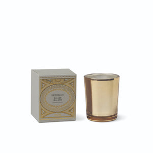 A square box with intricate gold-toned pattern designs next to a Silver Balsam Petite Candle gold glass vessel. - image 1