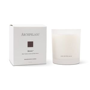 The Soho Boxed Candle, a white hand-poured candle in a frosted glass holder, is shown beside its matching labeled box. Made with a premium wax blend, it offers an elevated aromatic experience.1