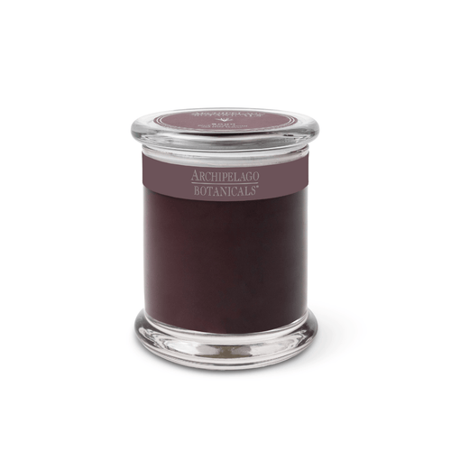 The Soho Jar Candle is a dark purple, hand-poured candle in a clear glass jar with a matching lid. Its label features "Archipelago Botanicals" in silver on a purple band, highlighting its premium wax blend for an elevated experience.
