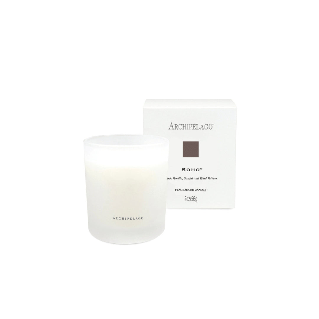 A Soho Petite Candle in a frosted glass holder sits before its matching box, featuring sophisticated black text and a brown square—capturing the timeless allure of a Carnaby Street speakeasy.1