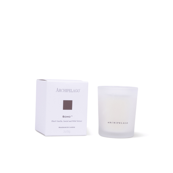 The Soho Petite Candle in a frosted glass jar sits next to its matching white box, featuring the signature Soho scent—black vanilla, sandal, and wild vetiver—making it an ideal stylish gift.