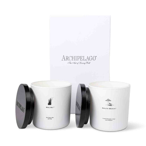 The Beaches Luxe Candle Gift Set features two white coconut wax candles, Malibu and South Beach, with black lids, placed before a white Archipelago box—an ideal gift for beach lovers and coastal home decor.