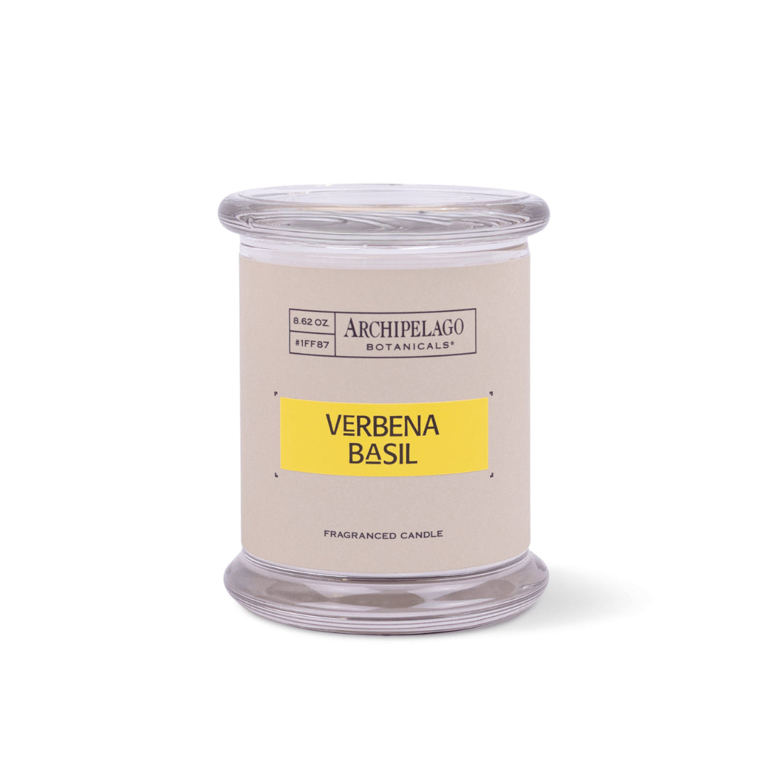 A clear glass jar candle with a beige label that reads "Archipelago Botanicals, Verbena Basil, Fragranced Candle." The label features a yellow section to highlight the scent on this elegant Verbena Basil Jar Candle.1