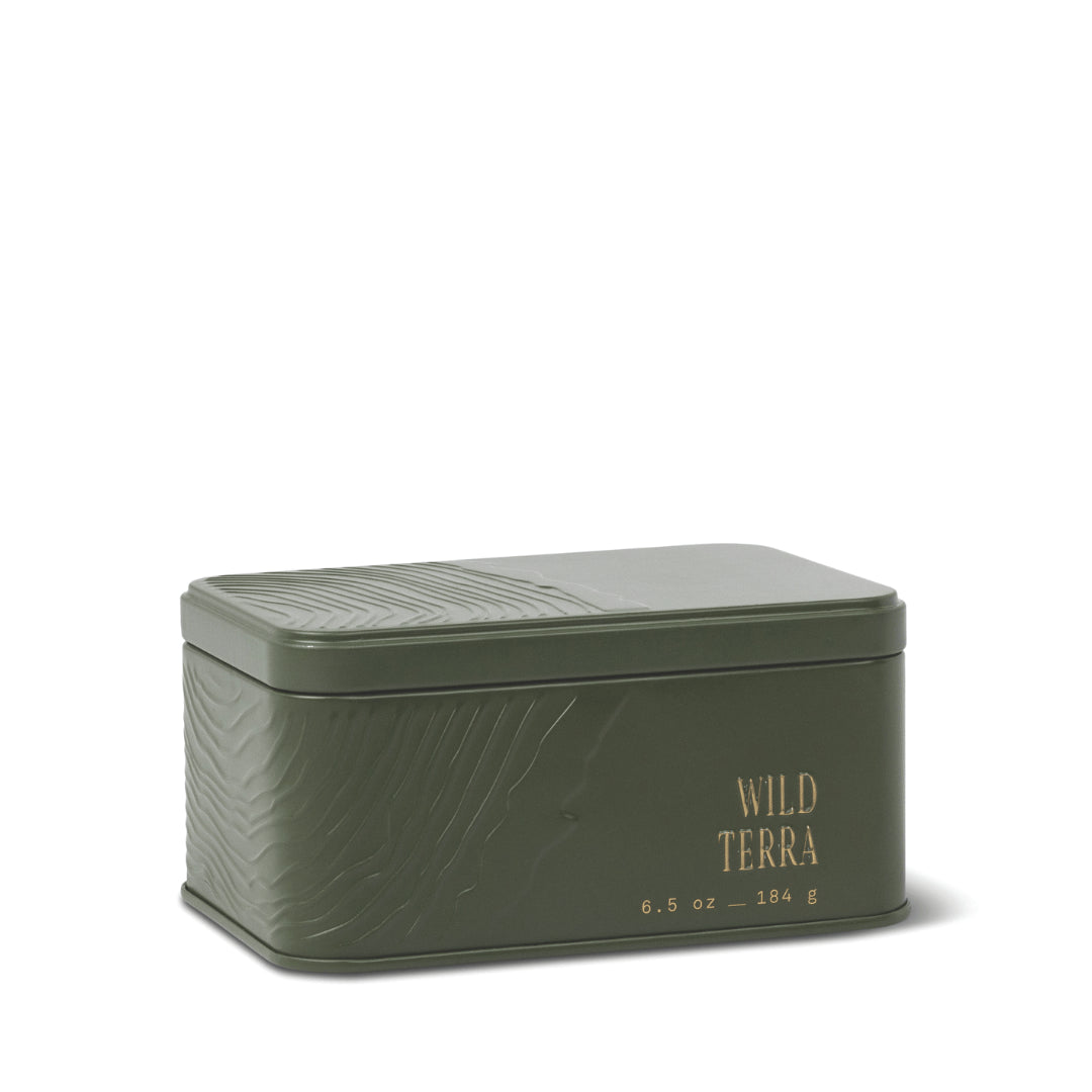 Rectangular green metal tin with embossed textured patterns, labeled Wild Terra Travel Tin Candle and 6.5 oz – 184 g in gold lettering on the front. The lid is closed, making this candle a convenient, portable fragrance option infused with subtle notes of cedarwood. - image 1