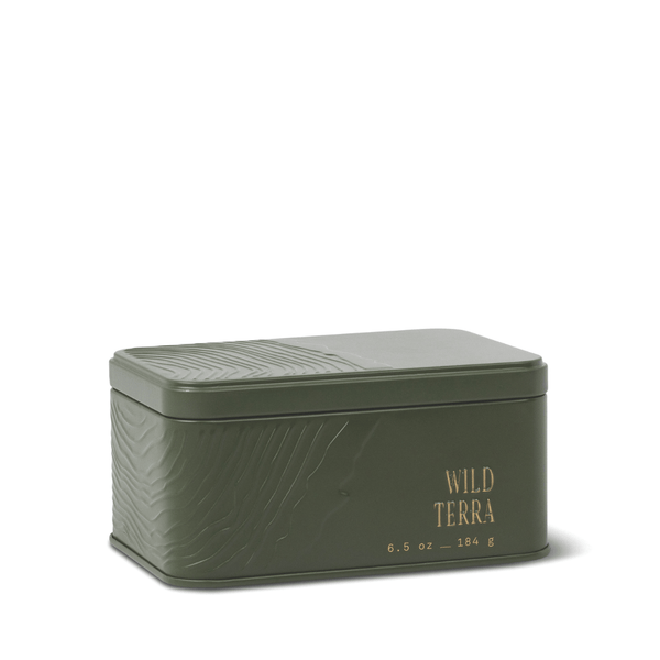 Rectangular green metal tin with embossed textured patterns, labeled Wild Terra Travel Tin Candle and 6.5 oz – 184 g in gold lettering on the front. The lid is closed, making this candle a convenient, portable fragrance option infused with subtle notes of cedarwood.