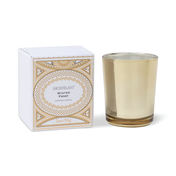 A Winter Frost Boxed Petite Candle featuring a square white box with intricate gold geometric patterns and a votive candle in a gold glass holder.