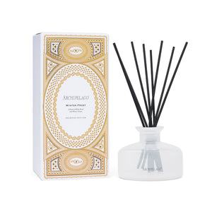 A Winter Frost reed diffuser with black reeds in a frosted glass bottle, next to its white box decorated with a gold, intricate geometric pattern. - image 1
