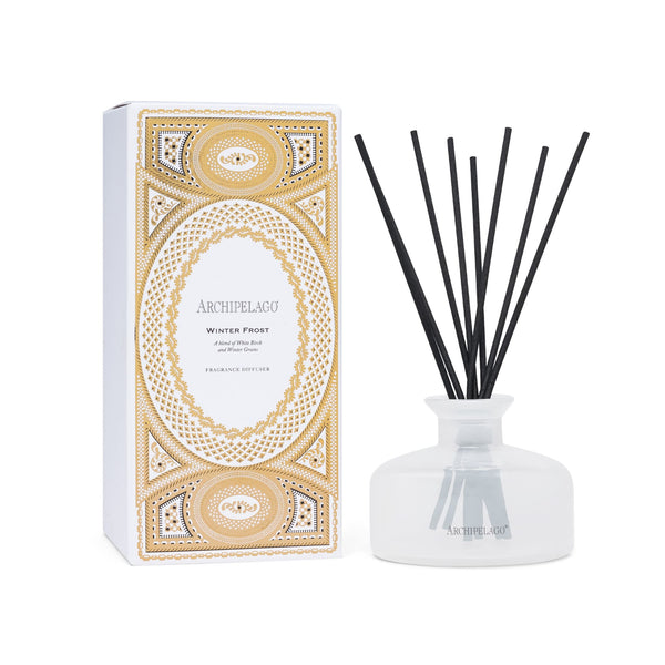 A Winter Frost reed diffuser with black reeds in a frosted glass bottle, next to its white box decorated with a gold, intricate geometric pattern.